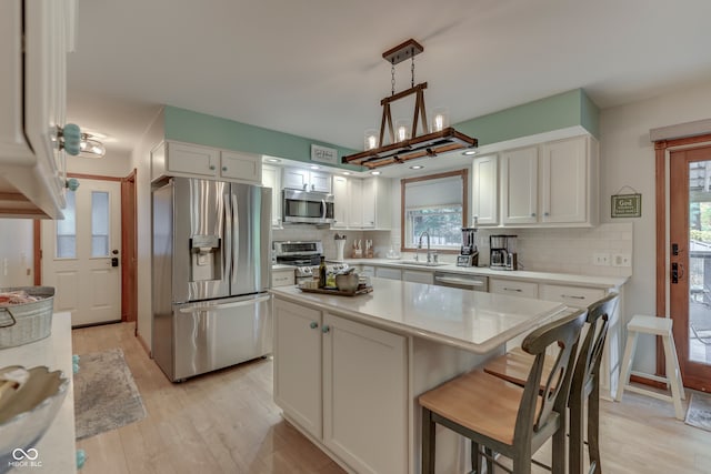 kitchen with white cabinets, hanging light fixtures, appliances with stainless steel finishes, light hardwood / wood-style flooring, and a center island