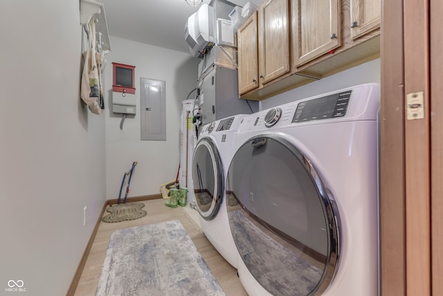 washroom featuring washing machine and dryer, light hardwood / wood-style floors, heating unit, cabinets, and electric panel