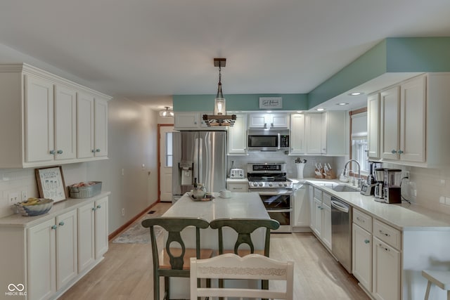 kitchen featuring sink, white cabinetry, stainless steel appliances, decorative light fixtures, and light hardwood / wood-style flooring