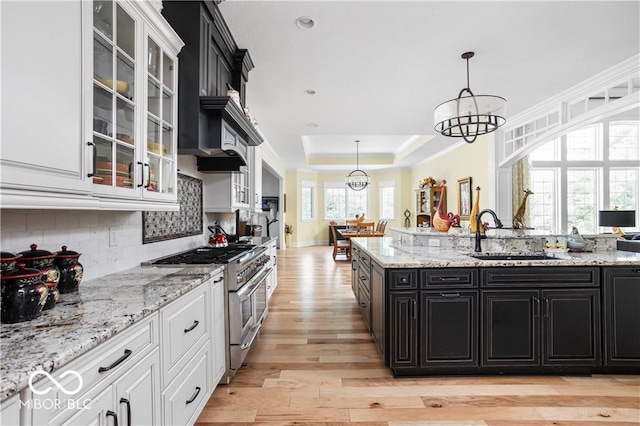 kitchen featuring range with two ovens, sink, an inviting chandelier, white cabinetry, and light hardwood / wood-style floors