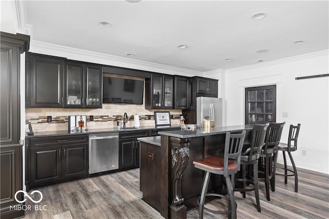 kitchen with light wood-type flooring, a kitchen island, stainless steel appliances, dark stone countertops, and ornamental molding