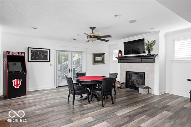 dining space with a tiled fireplace, ceiling fan, hardwood / wood-style flooring, ornamental molding, and french doors