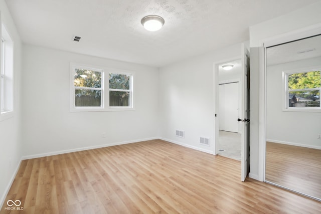 unfurnished bedroom featuring multiple windows, a textured ceiling, a closet, and light wood-type flooring