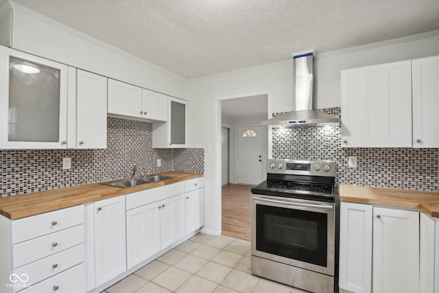 kitchen with wall chimney exhaust hood, sink, white cabinets, stainless steel range with electric cooktop, and butcher block countertops