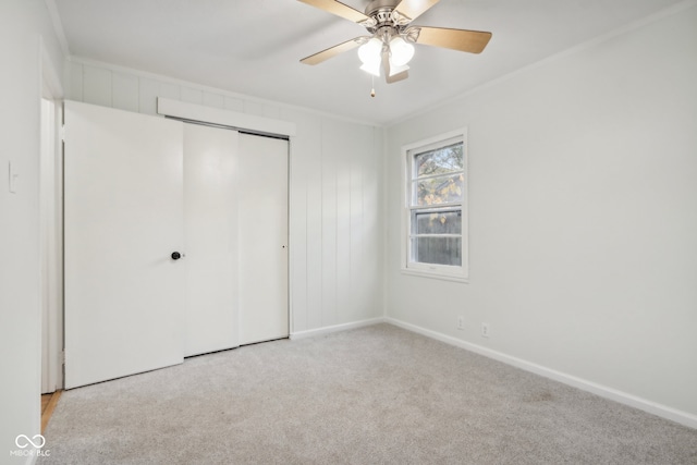 unfurnished bedroom featuring a closet, light colored carpet, crown molding, and ceiling fan