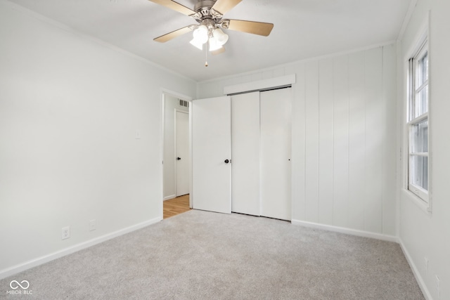 unfurnished bedroom featuring a closet, light colored carpet, crown molding, and ceiling fan