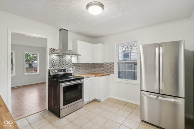 kitchen featuring a healthy amount of sunlight, appliances with stainless steel finishes, wall chimney range hood, and white cabinetry