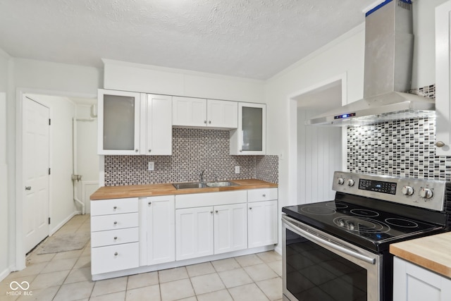 kitchen featuring wall chimney range hood, wood counters, sink, stainless steel electric range, and white cabinetry