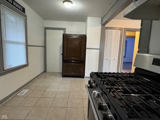 kitchen with stainless steel gas range oven, light tile patterned flooring, and dark brown cabinets