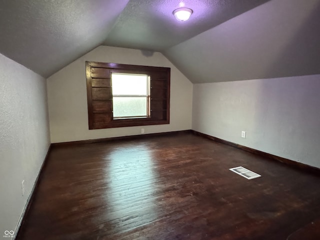 additional living space featuring a textured ceiling, vaulted ceiling, and dark hardwood / wood-style flooring