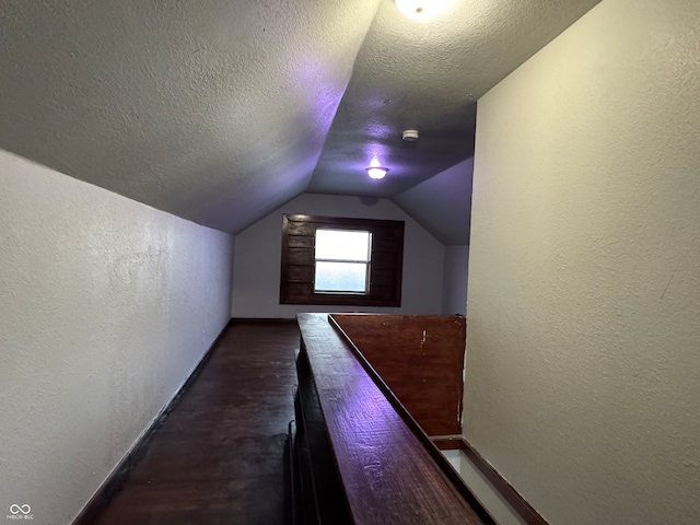 additional living space featuring vaulted ceiling, a textured ceiling, and dark hardwood / wood-style floors