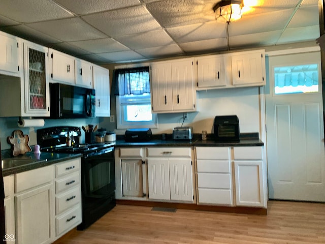 kitchen with black appliances, white cabinetry, a drop ceiling, and light hardwood / wood-style floors