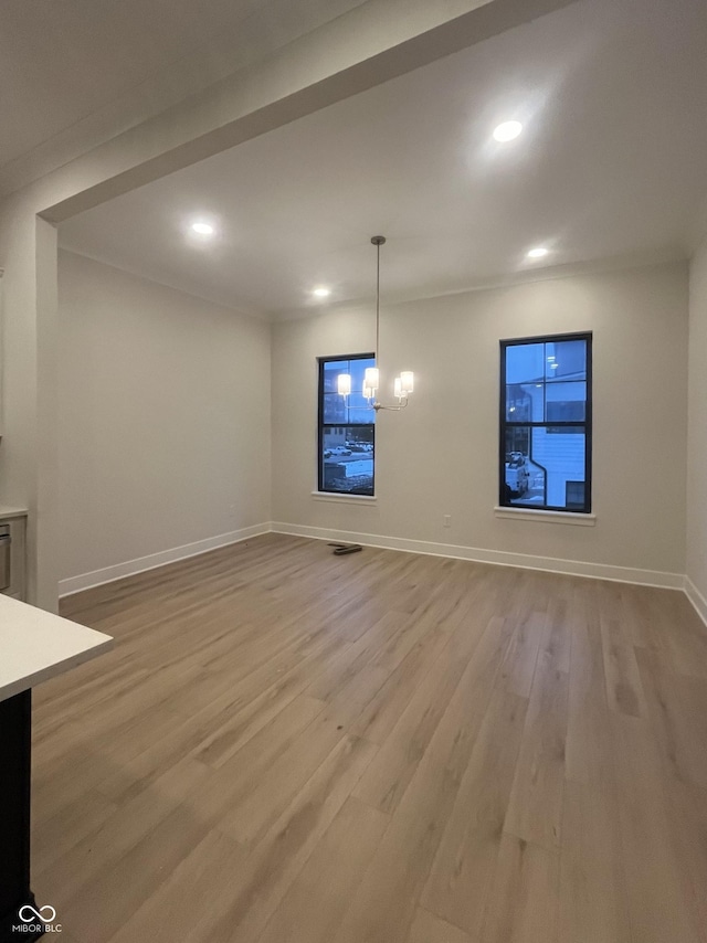 unfurnished living room featuring an inviting chandelier and light hardwood / wood-style floors