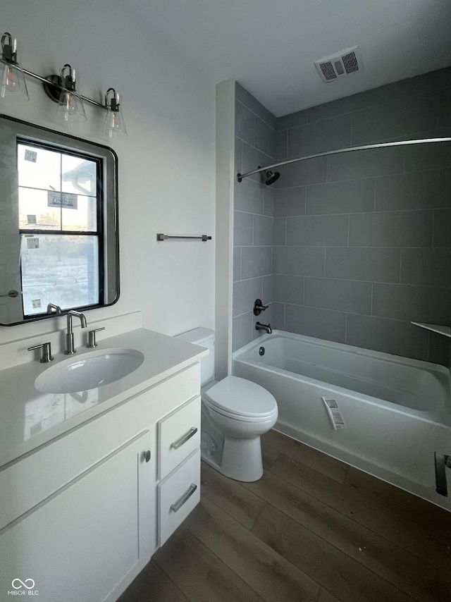 full bathroom featuring hardwood / wood-style flooring, vanity, tiled shower / bath, and toilet