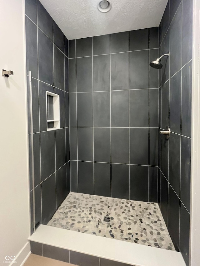 bathroom with a textured ceiling and a tile shower