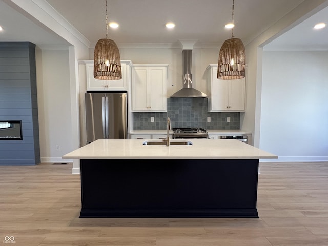 kitchen featuring a center island with sink, a sink, wall chimney range hood, appliances with stainless steel finishes, and light countertops