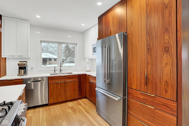 kitchen featuring sink, light hardwood / wood-style flooring, stainless steel appliances, decorative backsplash, and white cabinets