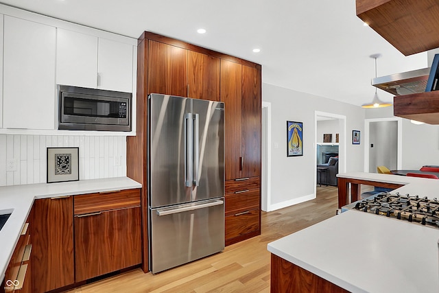 kitchen with white cabinetry, stainless steel appliances, hanging light fixtures, and light wood-type flooring