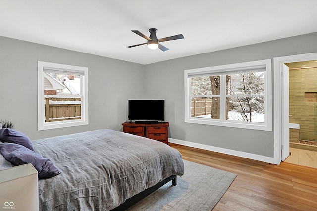 bedroom featuring ceiling fan, ensuite bathroom, multiple windows, and light hardwood / wood-style flooring