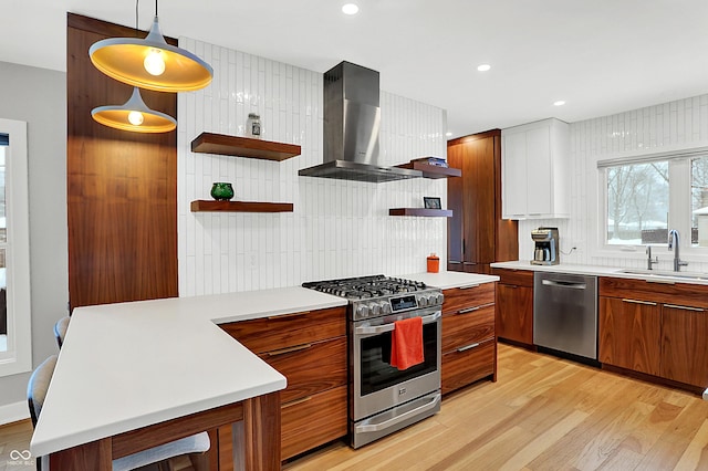 kitchen with sink, decorative light fixtures, light wood-type flooring, stainless steel appliances, and wall chimney range hood