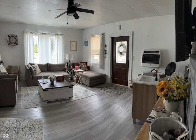 living room with heating unit, ceiling fan, light wood-type flooring, sink, and wooden walls