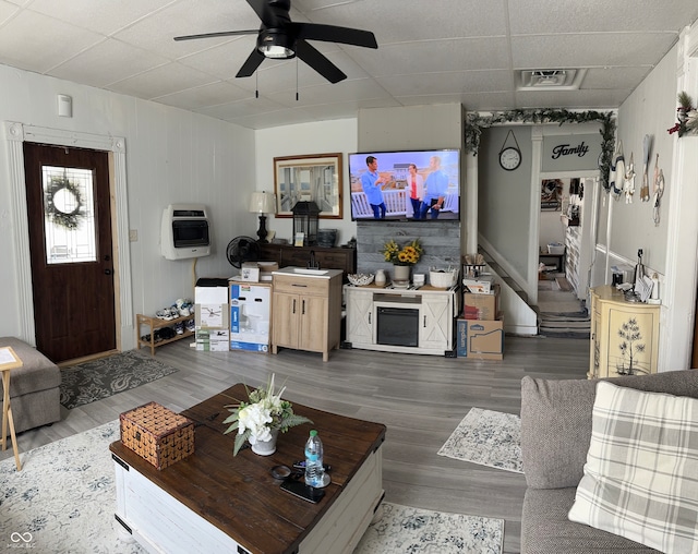 living room featuring ceiling fan, hardwood / wood-style flooring, heating unit, and wood walls