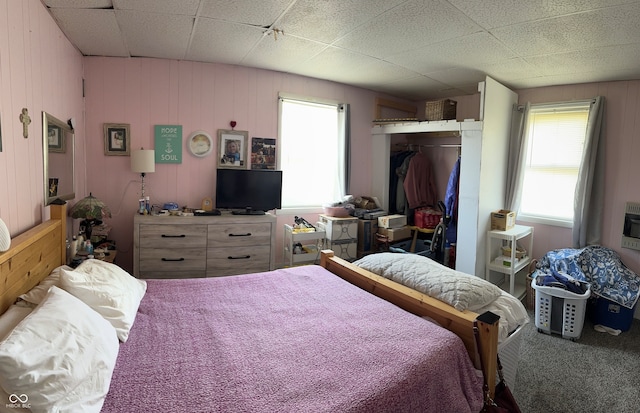 carpeted bedroom featuring a closet, a paneled ceiling, and wooden walls