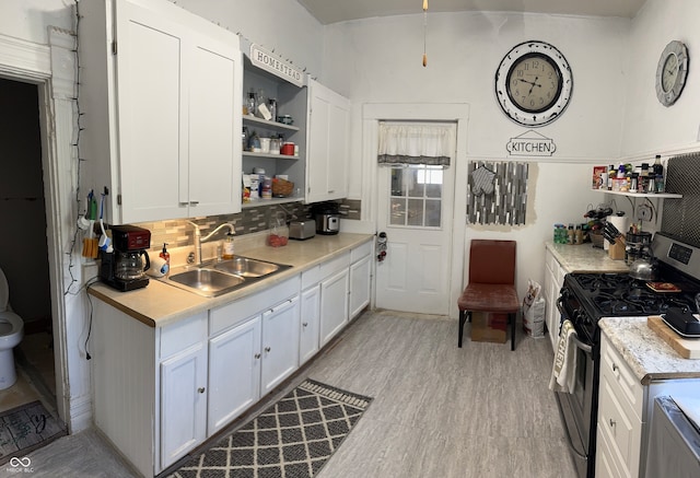 kitchen featuring tasteful backsplash, sink, stainless steel gas range oven, white cabinets, and light hardwood / wood-style flooring