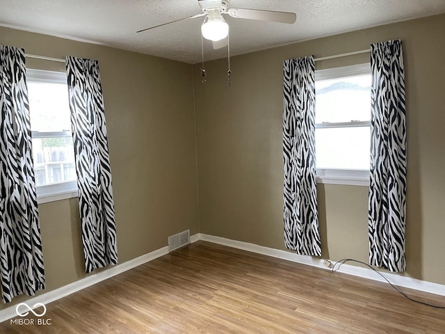 spare room featuring a ceiling fan, visible vents, a textured ceiling, and wood finished floors