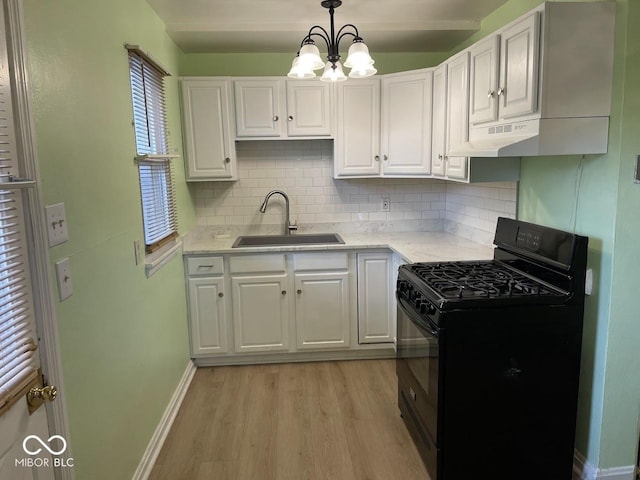 kitchen featuring a sink, under cabinet range hood, gas stove, white cabinetry, and light wood-style flooring