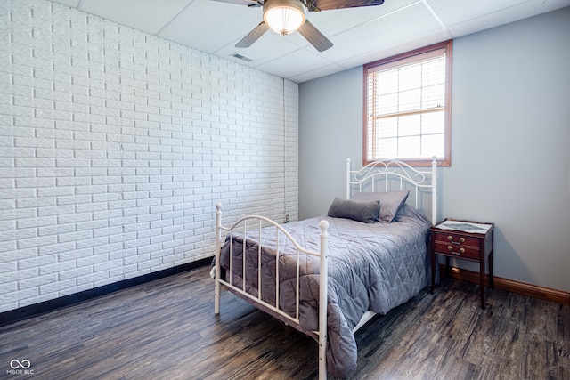 bedroom featuring dark wood-type flooring, ceiling fan, brick wall, and a paneled ceiling