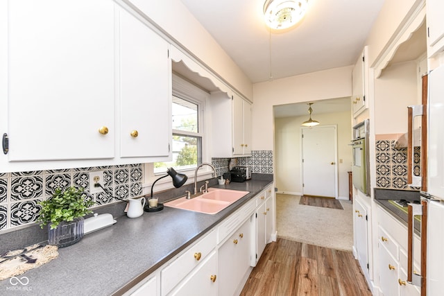 kitchen with white cabinets, sink, light wood-type flooring, and stainless steel oven