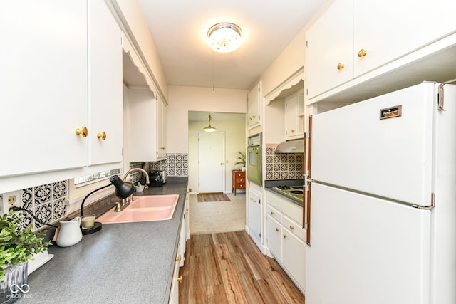 kitchen with sink, light wood-type flooring, stainless steel oven, white cabinetry, and white fridge