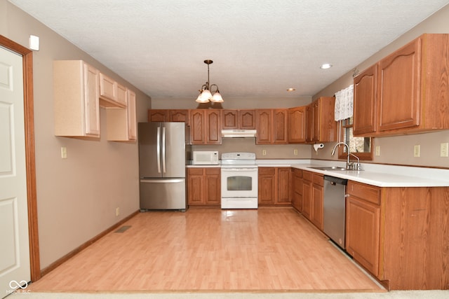 kitchen with pendant lighting, appliances with stainless steel finishes, sink, and light hardwood / wood-style flooring