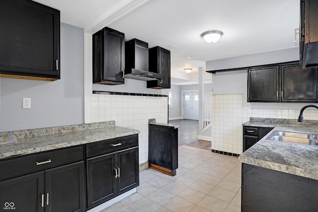 kitchen featuring light tile patterned floors, wall chimney range hood, sink, and tile walls