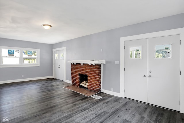 unfurnished living room featuring a fireplace, dark wood-type flooring, and plenty of natural light