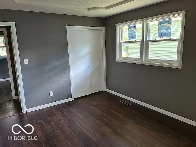 unfurnished bedroom featuring a closet, a textured ceiling, multiple windows, and dark hardwood / wood-style flooring