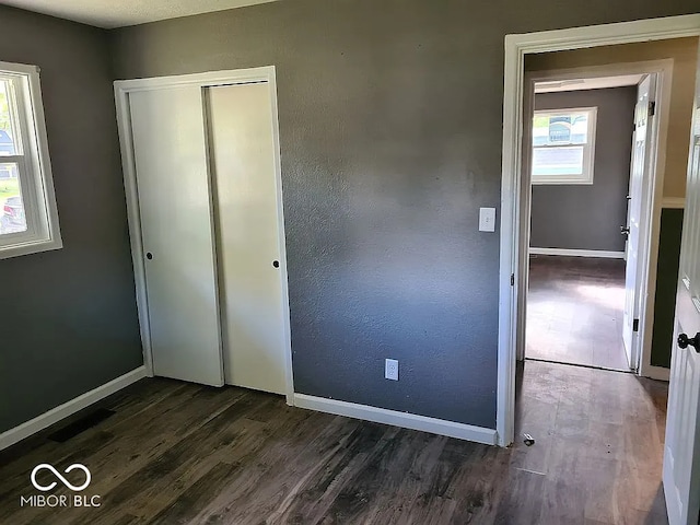 unfurnished bedroom featuring multiple windows, a closet, and dark hardwood / wood-style flooring