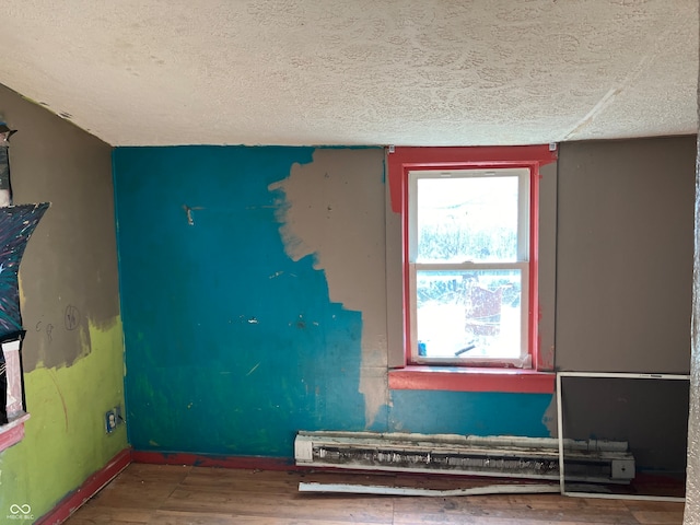 spare room with baseboard heating, a textured ceiling, and hardwood / wood-style flooring