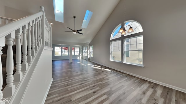 unfurnished living room with hardwood / wood-style flooring, high vaulted ceiling, a skylight, and ceiling fan with notable chandelier