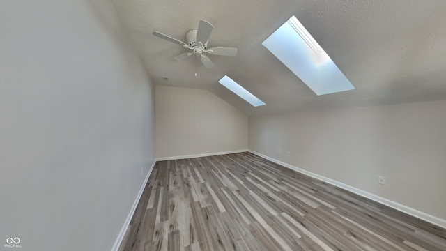 bonus room with ceiling fan, vaulted ceiling with skylight, and light wood-type flooring