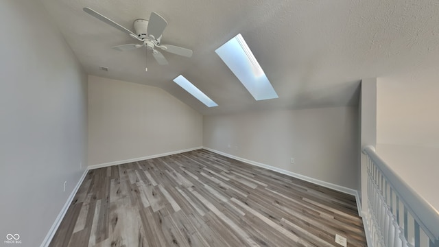 additional living space with light hardwood / wood-style floors, vaulted ceiling with skylight, and ceiling fan