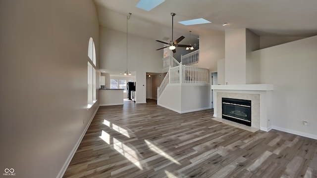 unfurnished living room featuring hardwood / wood-style floors, ceiling fan, and a skylight