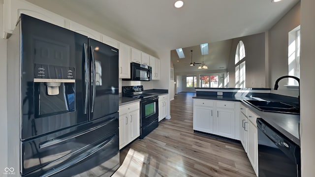 kitchen with black appliances, sink, a skylight, hardwood / wood-style floors, and white cabinetry