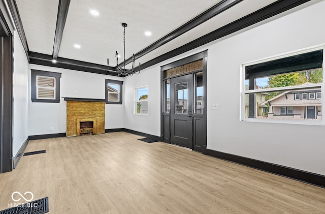 unfurnished living room featuring light hardwood / wood-style floors, beam ceiling, a wealth of natural light, and an inviting chandelier