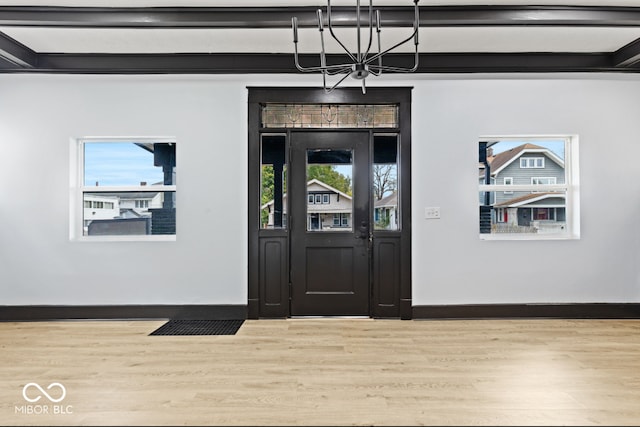 entrance foyer with beam ceiling, a wealth of natural light, an inviting chandelier, and hardwood / wood-style floors