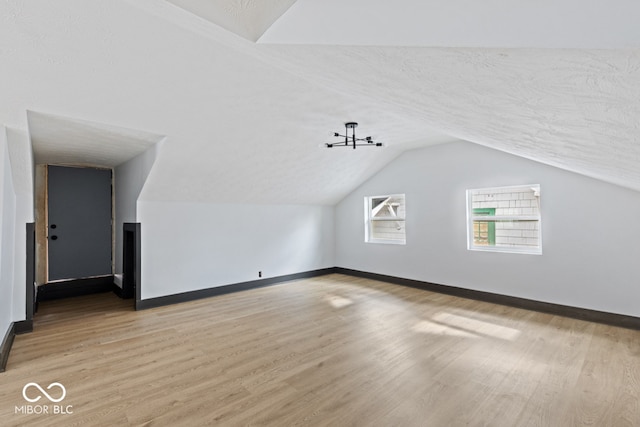 bonus room featuring a textured ceiling, light wood-type flooring, and vaulted ceiling