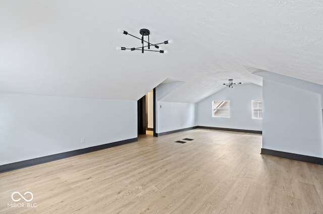 additional living space with light hardwood / wood-style floors, a textured ceiling, lofted ceiling, and a chandelier