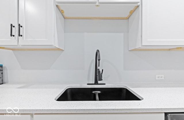 room details with white cabinetry, sink, and light stone counters