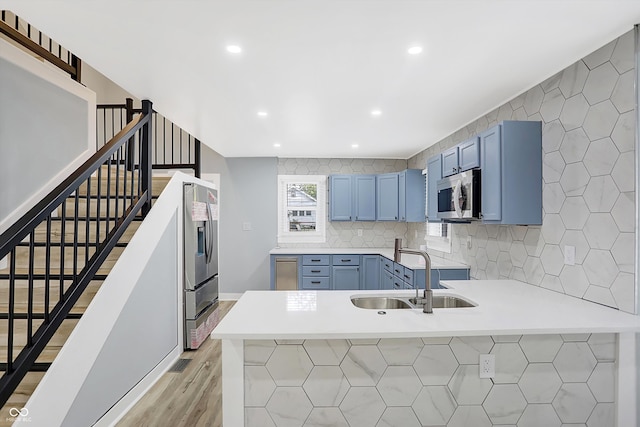 kitchen featuring sink, blue cabinets, kitchen peninsula, backsplash, and stainless steel appliances